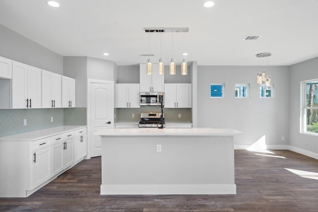 kitchen with white cabinetry, appliances with stainless steel finishes, a kitchen island with sink, and hanging light fixtures