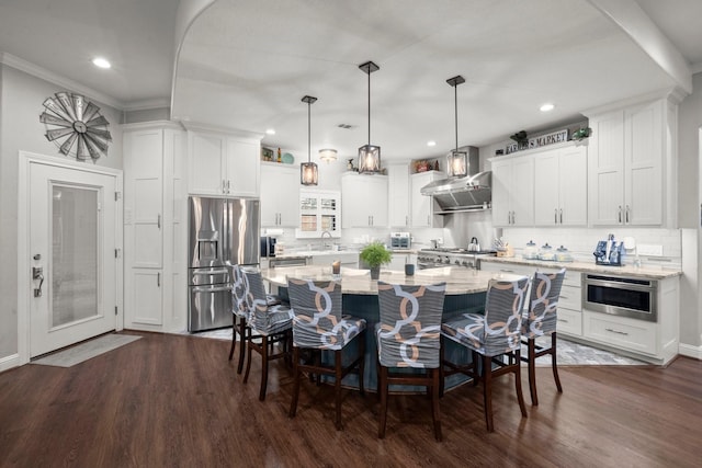 kitchen with a kitchen island, appliances with stainless steel finishes, white cabinets, hanging light fixtures, and wall chimney exhaust hood