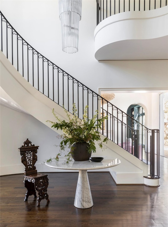 stairs with a towering ceiling, wood-type flooring, and a chandelier