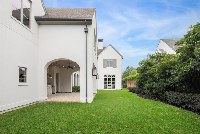 back of property with a lawn, a patio, ceiling fan, and an outdoor kitchen