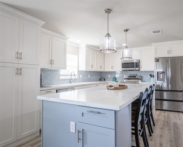 kitchen with stainless steel appliances, hanging light fixtures, a kitchen island, and white cabinets