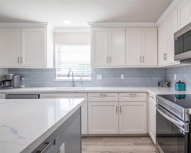 kitchen with light stone counters, ornamental molding, white cabinets, stainless steel appliances, and backsplash