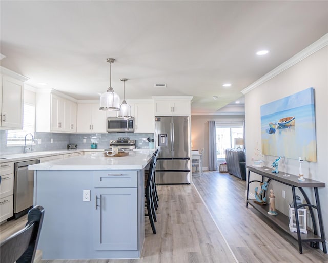 kitchen with pendant lighting, crown molding, stainless steel appliances, a center island, and white cabinets