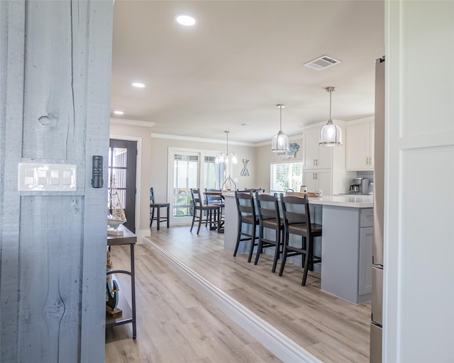 kitchen with ornamental molding, a breakfast bar, white cabinets, and decorative light fixtures