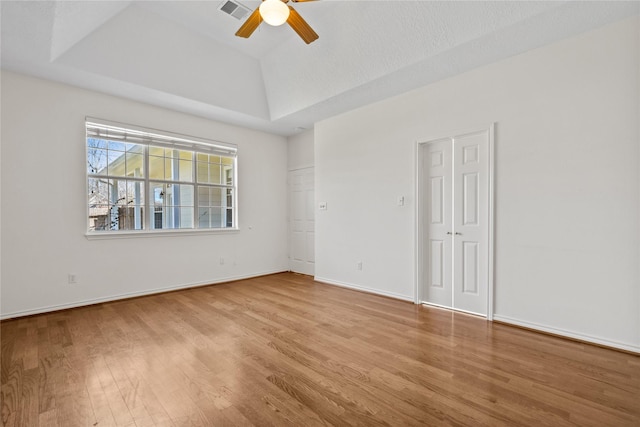 empty room featuring visible vents, a ceiling fan, vaulted ceiling, wood finished floors, and baseboards