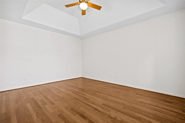 unfurnished room featuring a tray ceiling, ceiling fan, baseboards, and wood finished floors