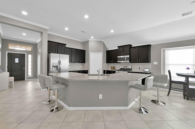 kitchen with stainless steel appliances, a kitchen island with sink, light tile patterned floors, and a kitchen bar