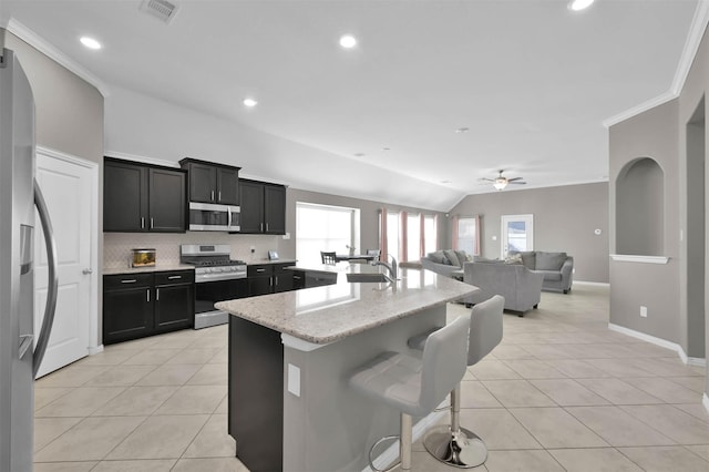 kitchen with a breakfast bar, stainless steel appliances, light stone counters, an island with sink, and light tile patterned flooring