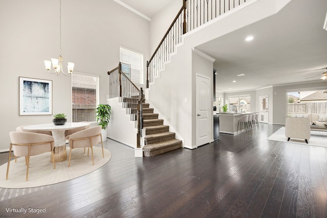 dining room with dark wood-type flooring, ornamental molding, ceiling fan with notable chandelier, and a high ceiling