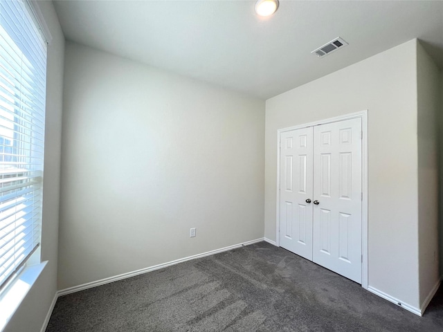 unfurnished bedroom with dark colored carpet and a closet