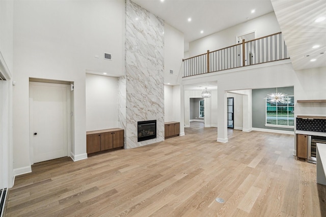 unfurnished living room featuring a high ceiling, wine cooler, a notable chandelier, a high end fireplace, and light wood-type flooring