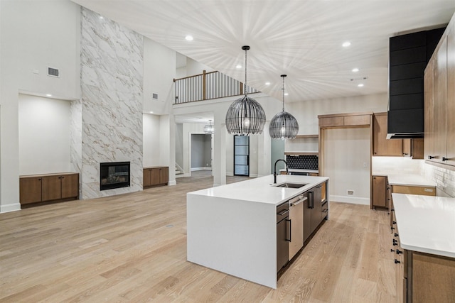 kitchen featuring a fireplace, decorative light fixtures, sink, a center island with sink, and light wood-type flooring