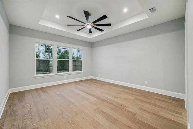 unfurnished room featuring ceiling fan, light wood-type flooring, and a tray ceiling