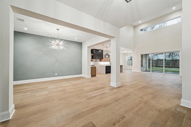 unfurnished living room featuring a high ceiling, a chandelier, and light hardwood / wood-style floors