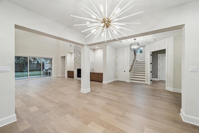 unfurnished living room featuring a high end fireplace, an inviting chandelier, and light wood-type flooring