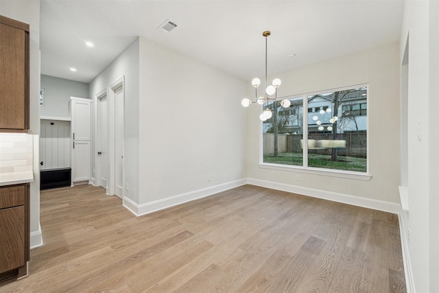 unfurnished dining area with a chandelier and light wood-type flooring