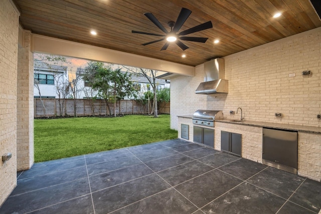 patio terrace at dusk with an outdoor kitchen, sink, a yard, ceiling fan, and a grill