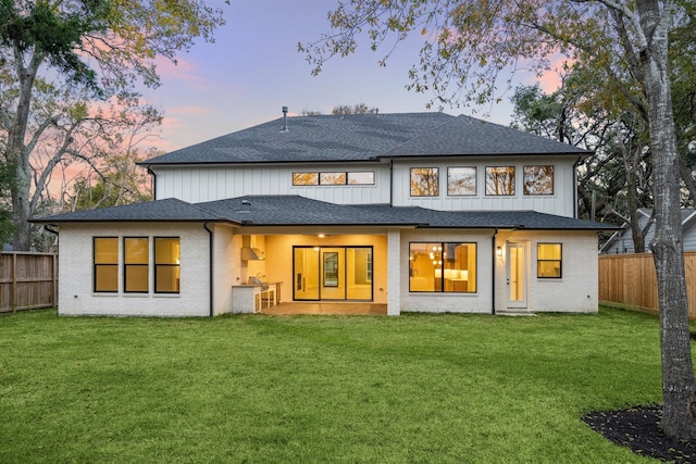 back house at dusk with a patio and a lawn