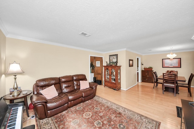 living room featuring ornamental molding, a notable chandelier, a textured ceiling, and light hardwood / wood-style flooring