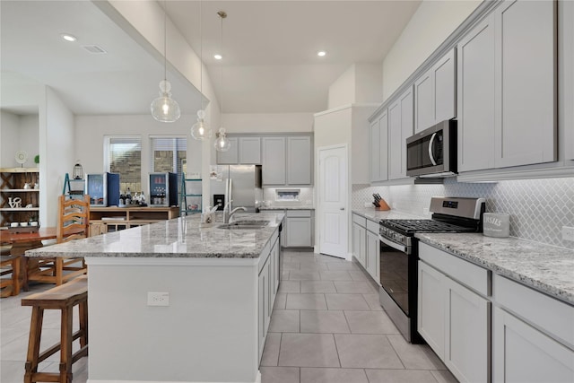 kitchen featuring decorative backsplash, an island with sink, appliances with stainless steel finishes, light stone counters, and a kitchen bar