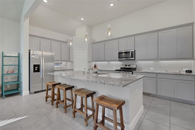 kitchen with appliances with stainless steel finishes, a sink, light stone counters, and gray cabinetry