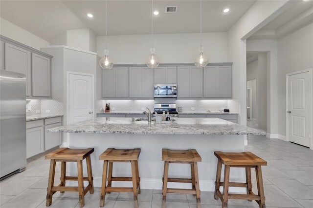 kitchen with gray cabinetry, stainless steel appliances, and an island with sink