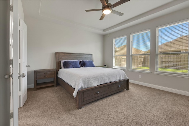 bedroom featuring light carpet, baseboards, a tray ceiling, and a ceiling fan