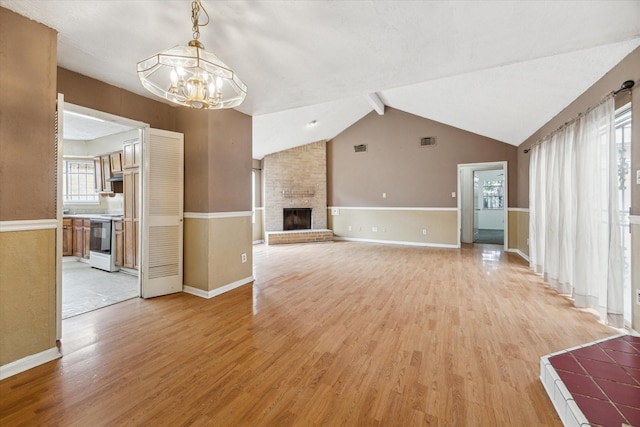 unfurnished living room with lofted ceiling with beams, a chandelier, light hardwood / wood-style floors, and a brick fireplace