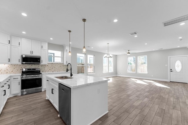 kitchen featuring pendant lighting, sink, appliances with stainless steel finishes, white cabinetry, and a kitchen island with sink