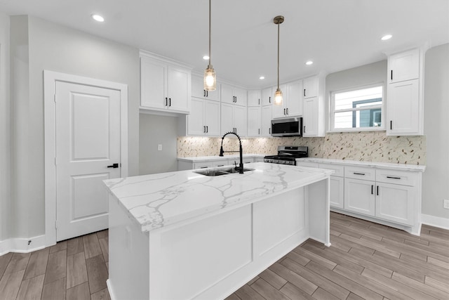 kitchen featuring white cabinetry, sink, a kitchen island with sink, stainless steel appliances, and light stone countertops