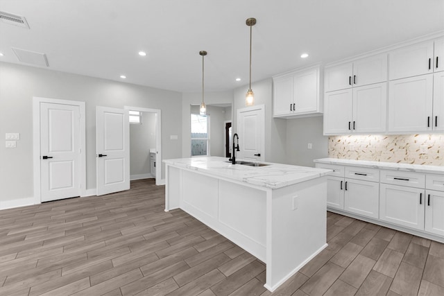 kitchen featuring sink, white cabinetry, light stone counters, an island with sink, and pendant lighting