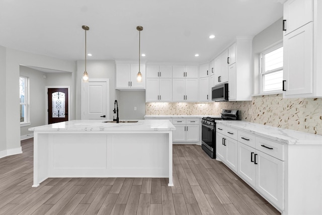 kitchen featuring appliances with stainless steel finishes, white cabinetry, hanging light fixtures, a kitchen island with sink, and light stone countertops