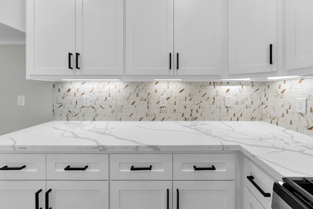 kitchen with white cabinetry, light stone counters, and stove