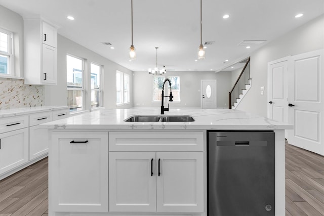 kitchen with pendant lighting, sink, dishwasher, white cabinetry, and a center island with sink