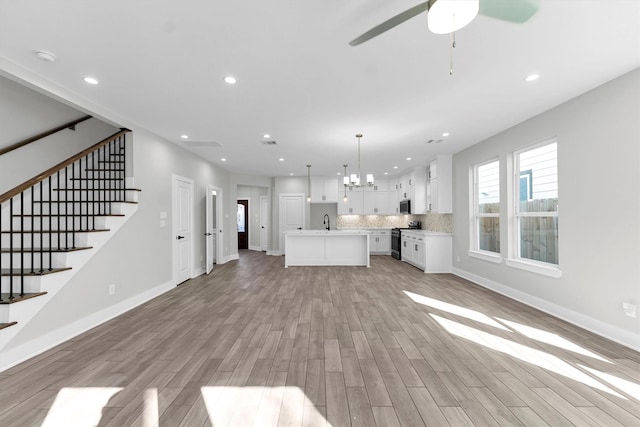 unfurnished living room with ceiling fan with notable chandelier, sink, and light hardwood / wood-style flooring