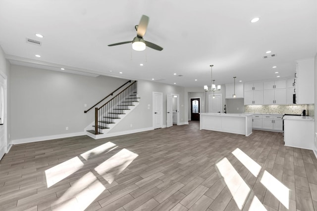 unfurnished living room featuring ceiling fan with notable chandelier and light hardwood / wood-style flooring