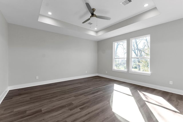 unfurnished room with ceiling fan, a tray ceiling, and dark hardwood / wood-style flooring