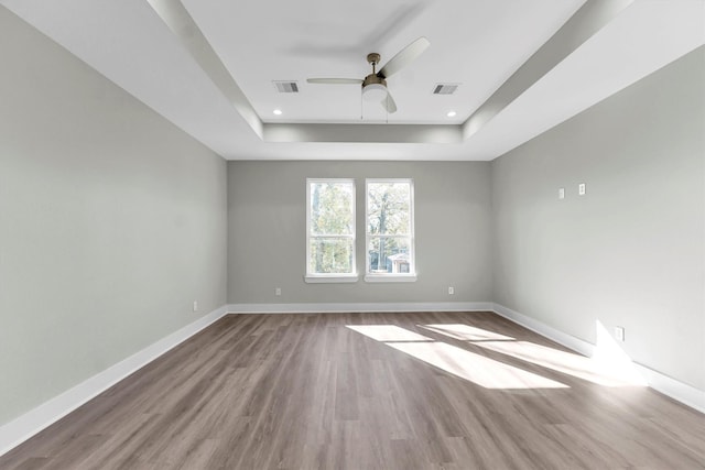 unfurnished room featuring a raised ceiling, ceiling fan, and light hardwood / wood-style floors