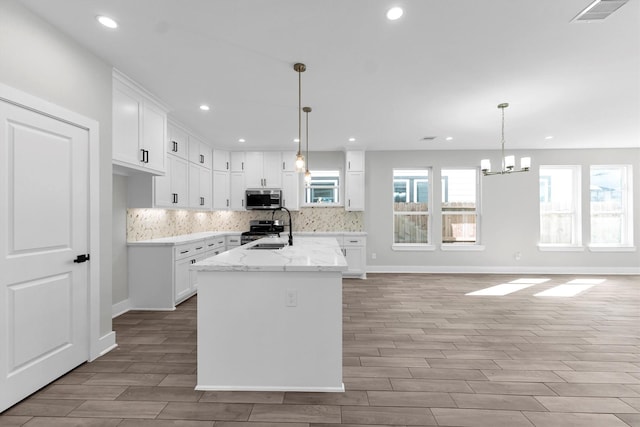 kitchen with stainless steel appliances, a kitchen island with sink, white cabinets, and light stone counters