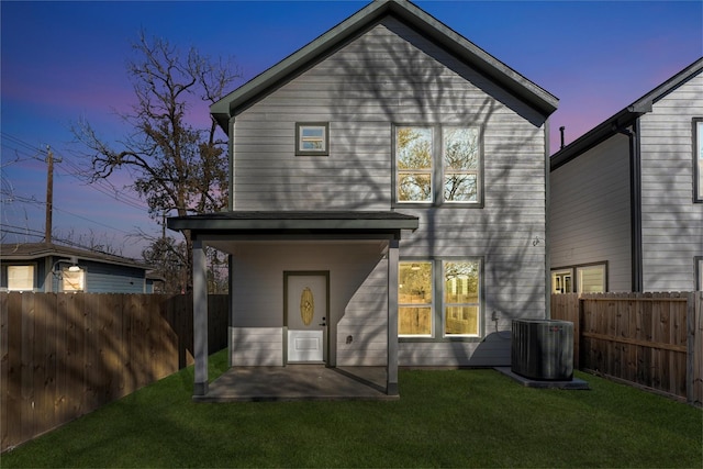 back house at dusk featuring central AC unit, a patio area, and a lawn