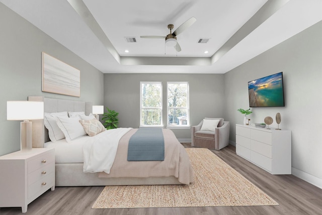 bedroom featuring ceiling fan, a raised ceiling, and light wood-type flooring