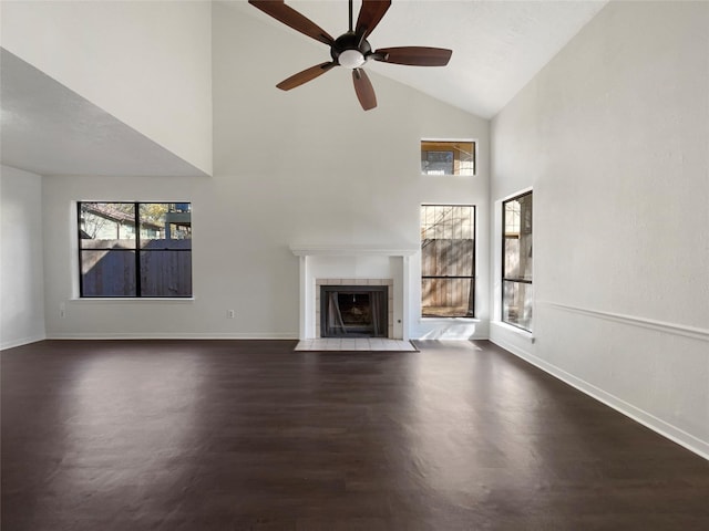 unfurnished living room featuring dark wood-type flooring, ceiling fan, a tiled fireplace, and high vaulted ceiling