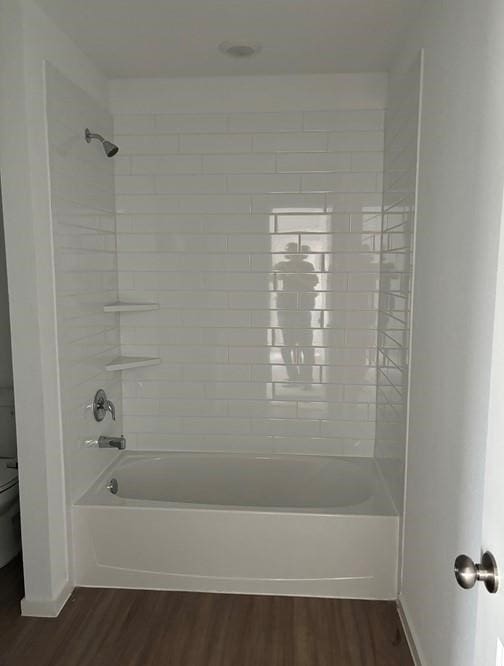 bathroom featuring hardwood / wood-style flooring, tiled shower / bath, and toilet