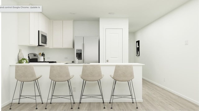 kitchen featuring white cabinetry, appliances with stainless steel finishes, a kitchen bar, and light hardwood / wood-style floors