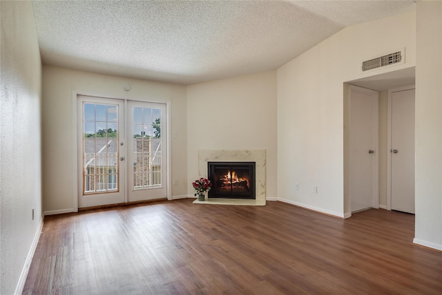 unfurnished living room with hardwood / wood-style flooring, a high end fireplace, a textured ceiling, vaulted ceiling, and french doors