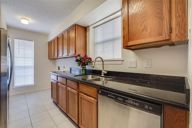 kitchen with sink, dark stone counters, light tile patterned floors, stainless steel appliances, and a textured ceiling