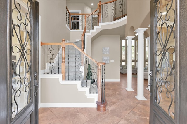 foyer entrance with a towering ceiling, tile patterned floors, and ornate columns