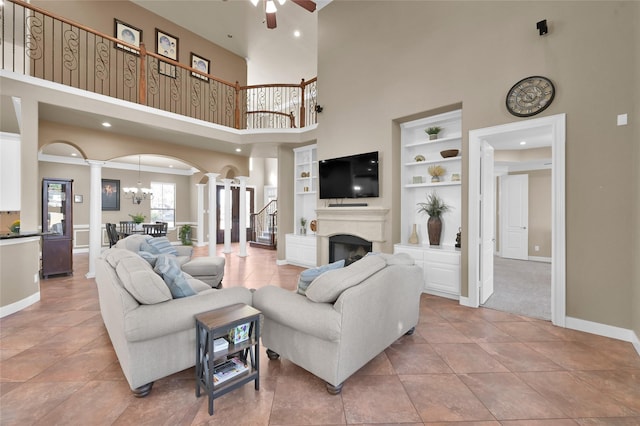 tiled living room featuring ceiling fan, decorative columns, built in features, and a towering ceiling