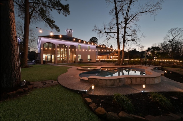 pool at dusk featuring a patio area, a lawn, and an in ground hot tub