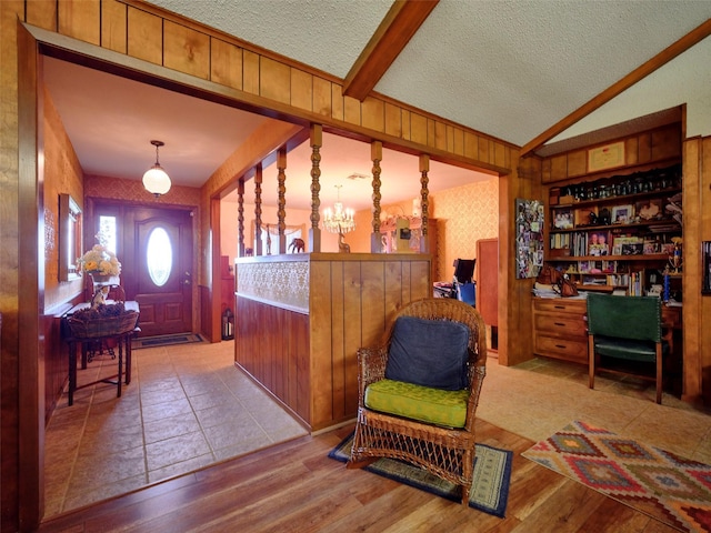 interior space featuring an inviting chandelier, vaulted ceiling with beams, wooden walls, a textured ceiling, and light wood-type flooring